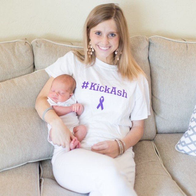 Ashleigh holding a newborn while wearing a #KickAsh brain cancer awareness shirt.